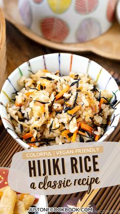 a bowl filled with rice and carrots on top of a wooden table next to other plates