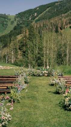 an empty park with benches and flowers in the foreground, surrounded by trees and mountains