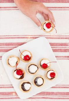 small desserts with cherries and whipped cream are on a white plate next to a person's hand