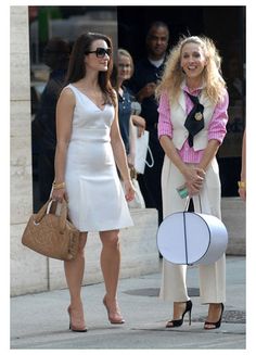 two women in white dresses are talking to each other on the street while one woman is holding a large object