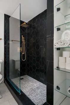 a black and white bathroom with hexagonal tiles on the floor, glass shower door, and toilet