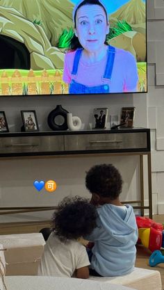 two children sitting in front of a flat screen tv with an image of a woman on it