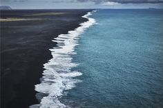 an aerial view of the black sand beach with waves coming in from the shore and dark blue water