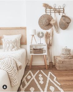 a bedroom with white walls and wooden flooring has baskets on the wall above the bed