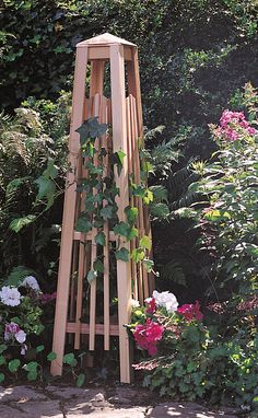 a wooden tower with plants growing on it in the middle of some bushes and flowers