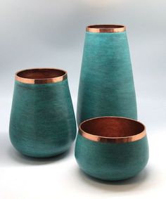 three teal vases with copper rims are shown in front of a white background