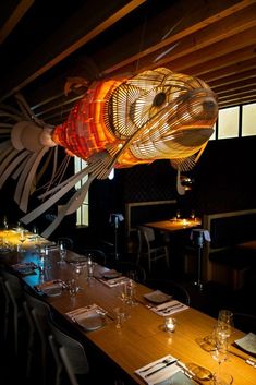 a dining room table is set with place settings and an art piece hanging from the ceiling