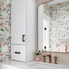 a bathroom with floral wallpaper and white cabinetry next to a mirror on the wall