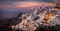 the white buildings are lit up at night on the cliff above the water in this photo