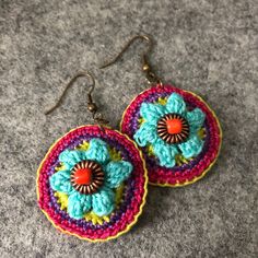 two crocheted earrings with orange, blue and pink flowers are on a gray surface