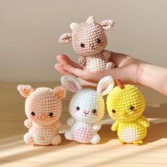 three small crocheted animals sitting next to each other on a wooden table in front of a person's hand