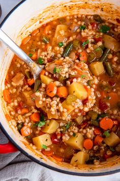 a pot filled with soup and vegetables on top of a table next to a spoon