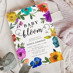 a baby is bloom card on top of a blanket next to some plants and flowers