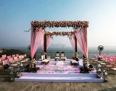 an outdoor wedding set up with pink and white flowers on the stage, overlooking the ocean