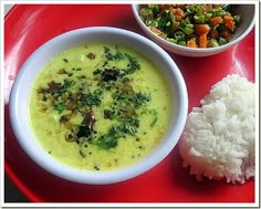 a bowl of soup, rice and vegetables on a red plate with a side dish