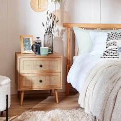 a bed room with a neatly made bed next to a wooden dresser and a potted plant