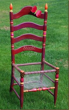 a red chair sitting in the grass with two candles on top of it's back