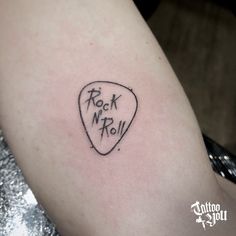 a rock n roll guitar pick tattoo on the right arm and shoulder, with words written in cursive ink