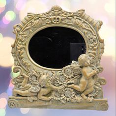 an ornate mirror with cherubs and flowers on it in front of a blurry background