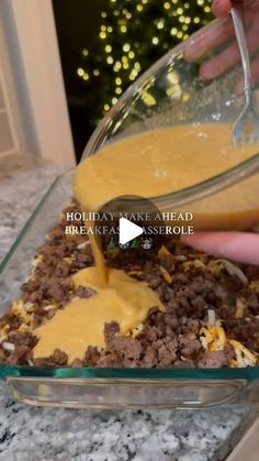 someone is pouring sauce on some food in a glass casserole dish with ground beef and cheese