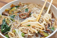 a white bowl filled with noodles, meat and vegetables on top of a wooden table