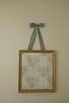 a painting hanging on the wall with a bow around it's neck and an empty frame