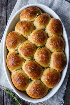 a white bowl filled with bread rolls on top of a wooden table next to a napkin