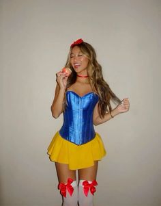 a woman in a blue and yellow corset holding an apple while standing next to a wall