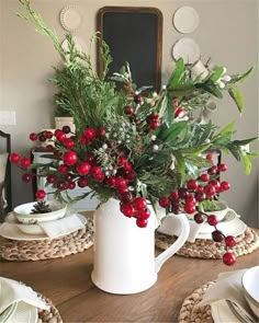 a white pitcher filled with berries and greenery on top of a dining room table