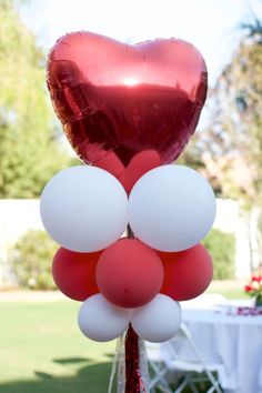 red and white balloons are arranged in the shape of a heart on top of a pole