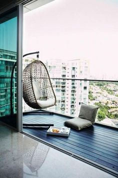 a balcony with a hanging chair and pillows on the floor next to a glass door