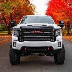 the front end of a white gmc truck parked on a street with trees in the background