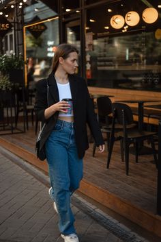 a woman is walking down the street with her cell phone in her hand and wearing jeans