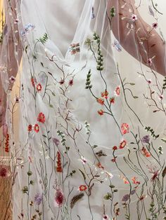 a woman wearing a white dress with flowers on it and sheer fabric over her shoulders