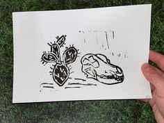 a hand holding up a piece of paper with a drawing of a dog and cactus on it