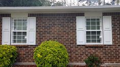 a brick house with white windows and bushes