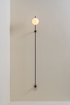 a white wall with a black pole and a light on it's side in the corner