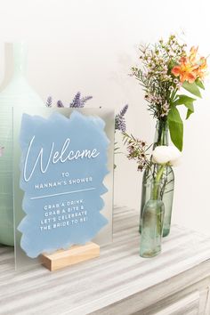 a welcome sign and vase with flowers on a mantle