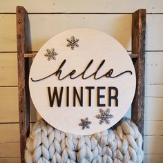 a wooden sign that says hello winter sitting on top of a pile of knits