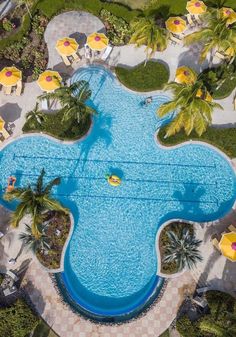 an aerial view of a swimming pool surrounded by palm trees and lawn chairs with umbrellas