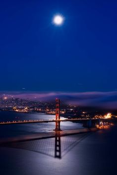 the golden gate bridge is lit up at night, with the moon in the background