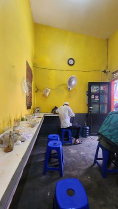 a man sitting at a table in a room with yellow walls and blue stools