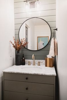 a bathroom vanity with a round mirror above it and flowers in vases on the counter