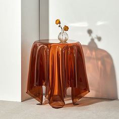 a vase with flowers sitting on top of a small table next to a white wall