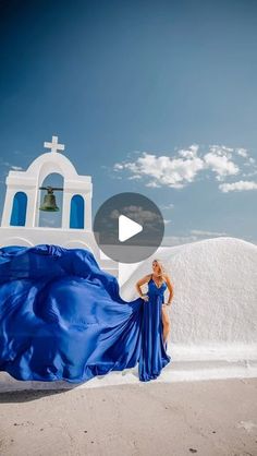 a woman in a blue dress is standing near a white church with a bell tower