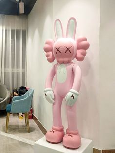 an inflatable pink bunny standing on top of a white pedestal next to a blue chair