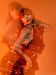 two beautiful women standing next to each other in front of an orange background and one is wearing a shiny dress