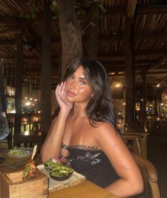 a woman sitting at a table with a bowl of food in front of her face