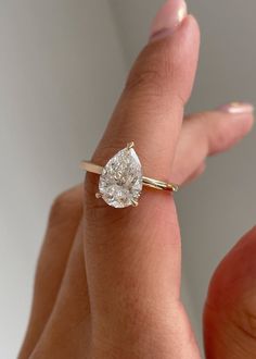 a woman's hand holding a ring with a pear shaped diamond on it,