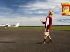 a young boy standing on top of an airport tarmac holding a cell phone in his hand